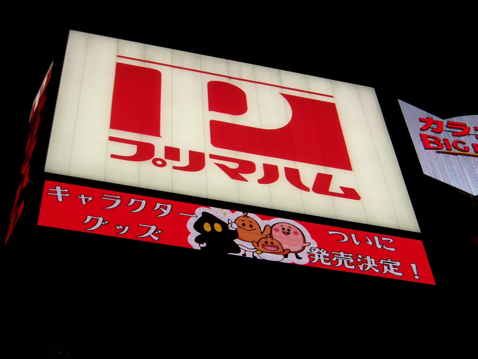 A bright Japanese storefront sign photographed at night.